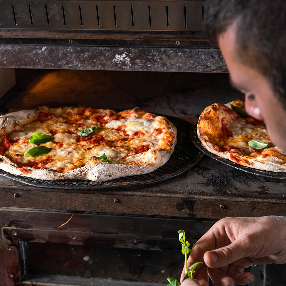 בחור שם בזיליקום טרי על פיצה שנכנסת לטאבון