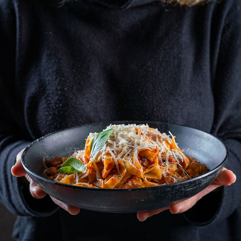 בחור מחזיק בשתי ידיים קערת פסטה עם פרמזן מגורר מעל