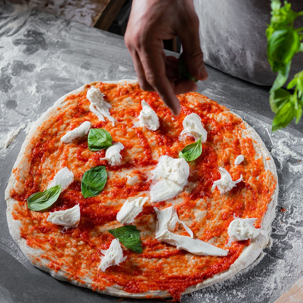 יד מפזרת עלי בזיליקום על פיצה עם קרעי מוצרלה